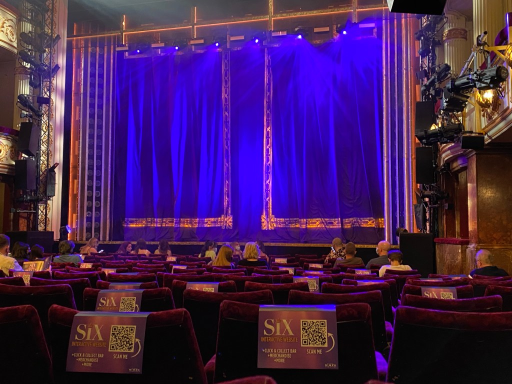 Socially distanced performance of Six: The Musical. Chairs with the cardboard sign remained empty. About half the chairs in the picture are marked with signs.