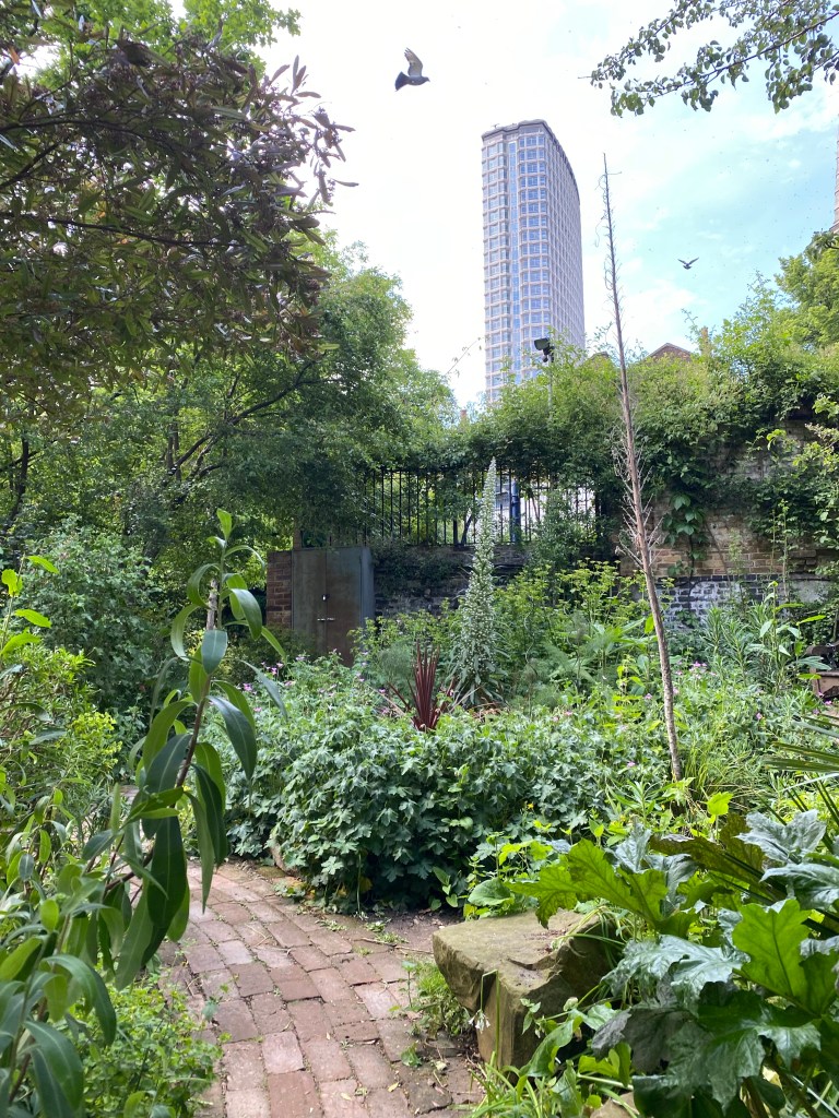 Skyscraper in the background, pigeon flying on the left, and green garden with a red brick path in the foreground.