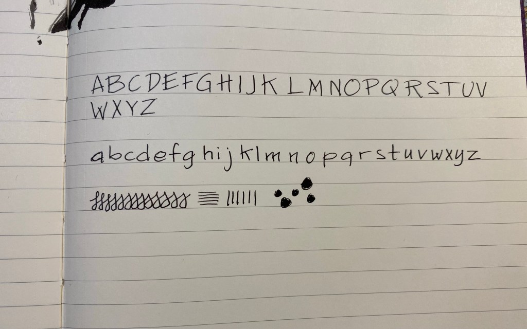 Page with alphabet handwritten in black ink once in uppercase and once in lowecase with an ink smudge on the top left. 