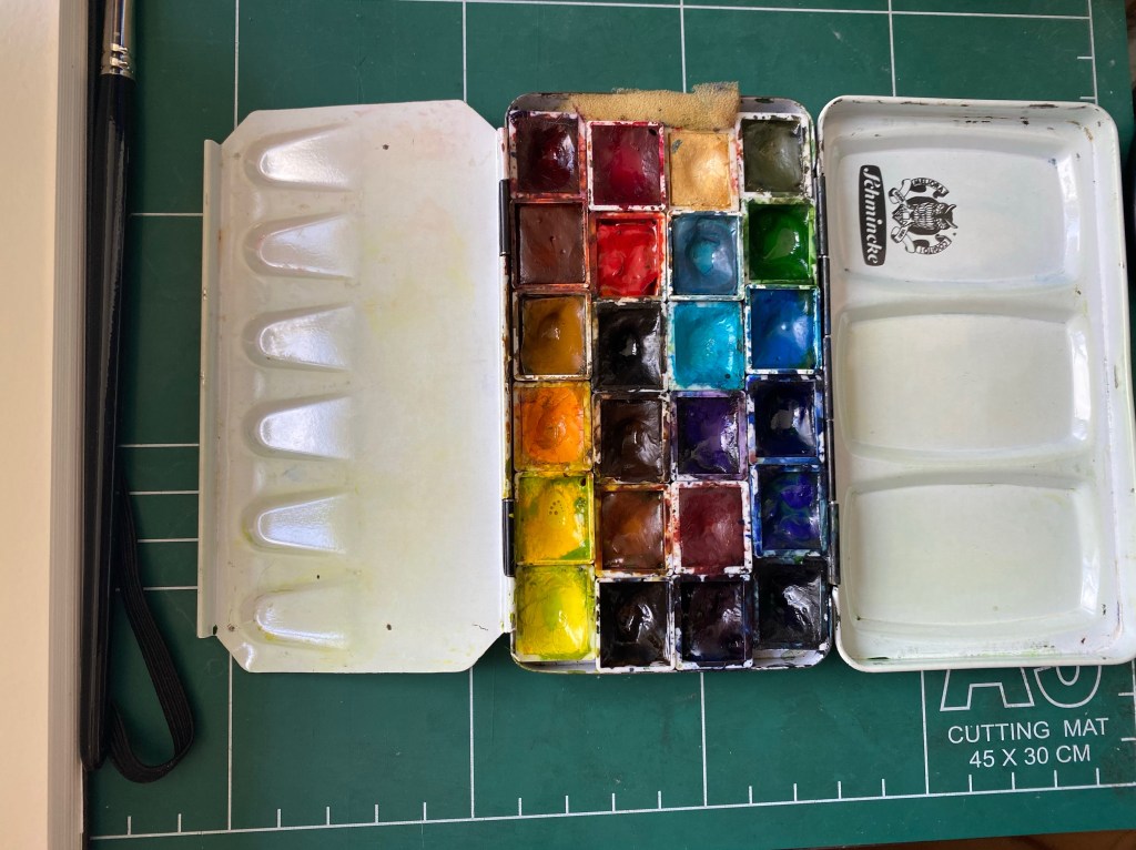 Metal watercolour tin filled with half pans of paint.